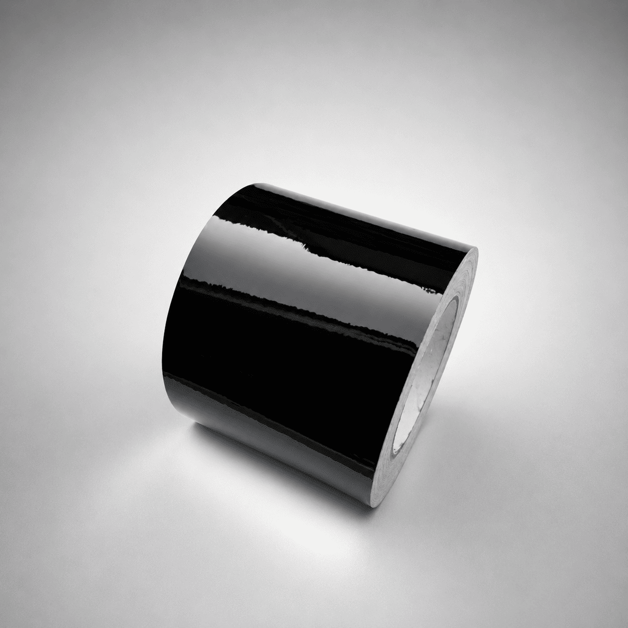 A roll of glossy black tape, shown at an angle on a neutral gray background.