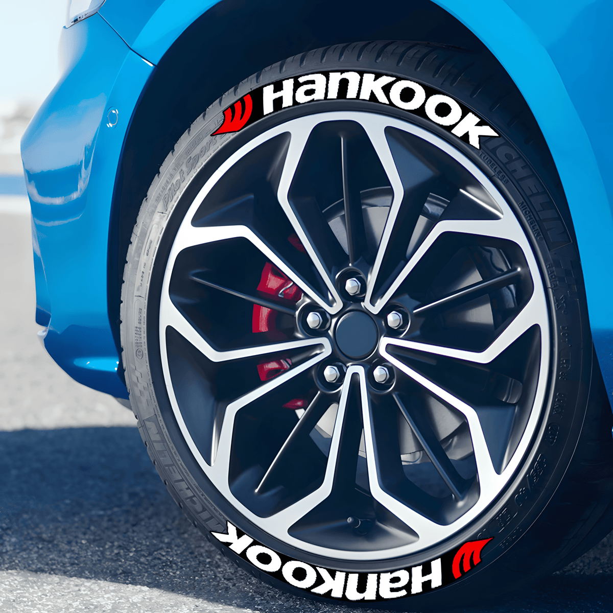 Close-up of a blue sports car with ChroMorpher Hankook 3D Tire Lettering applied on the tires, featuring bold white text with a red logo. The decals enhance the wheel's sporty look, adding a high-performance touch to the vehicle.