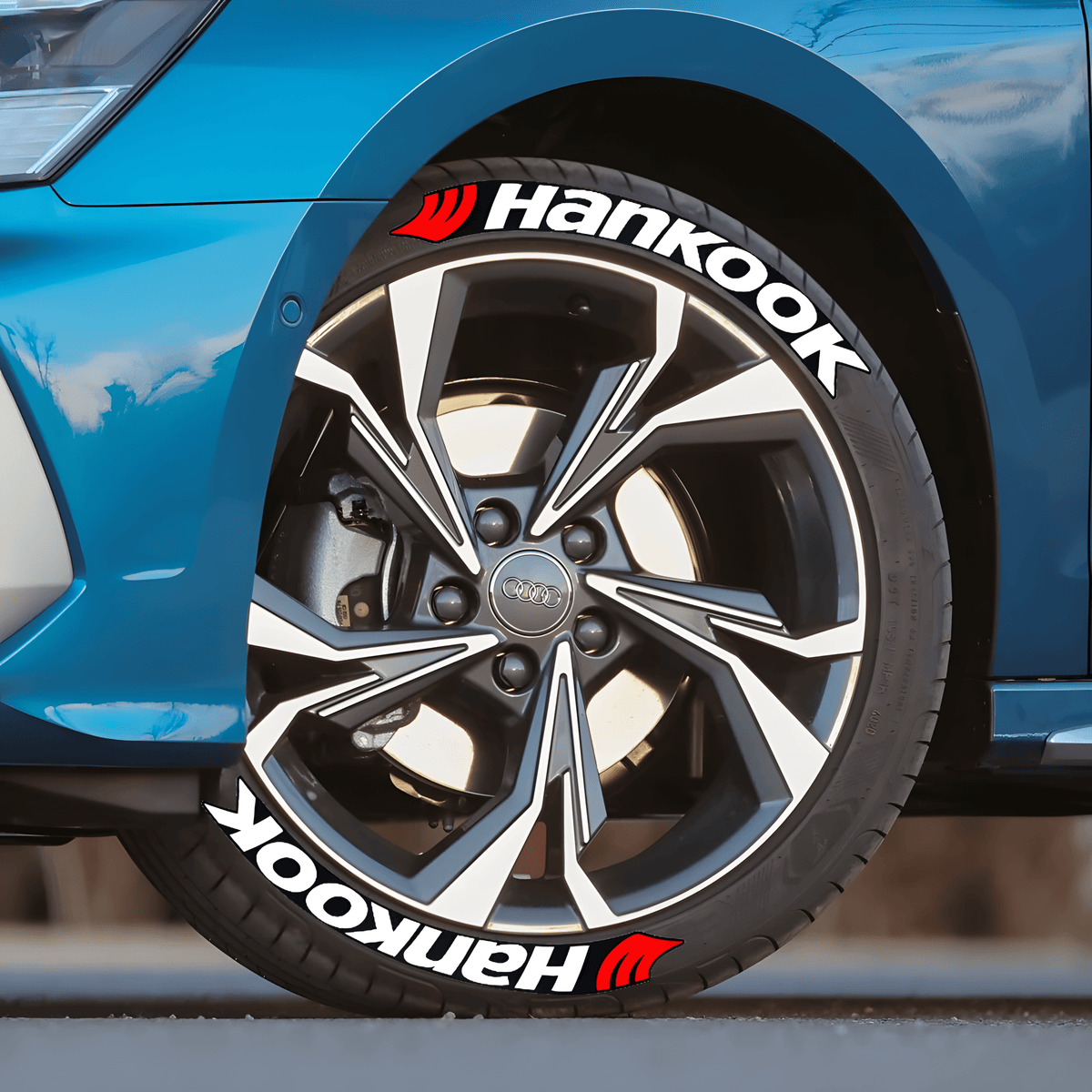 Close-up of an Audi wheel featuring ChroMorpher Hankook 3D Tire Lettering, showcasing bold white lettering with a red logo. The tire decals enhance the sporty and aggressive aesthetic of the car, making it stand out with a race-inspired look.