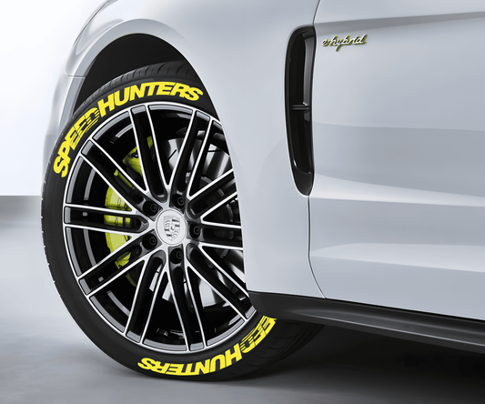 A white Porsche e-Hybrid featuring ChroMorpher SpeedHunters Yellow 3D Tire Lettering Decals on its black tires. The vibrant yellow SpeedHunters text perfectly matches the neon yellow brake calipers, creating a bold and high-performance look that enhances the sporty appeal of the luxury vehicle.