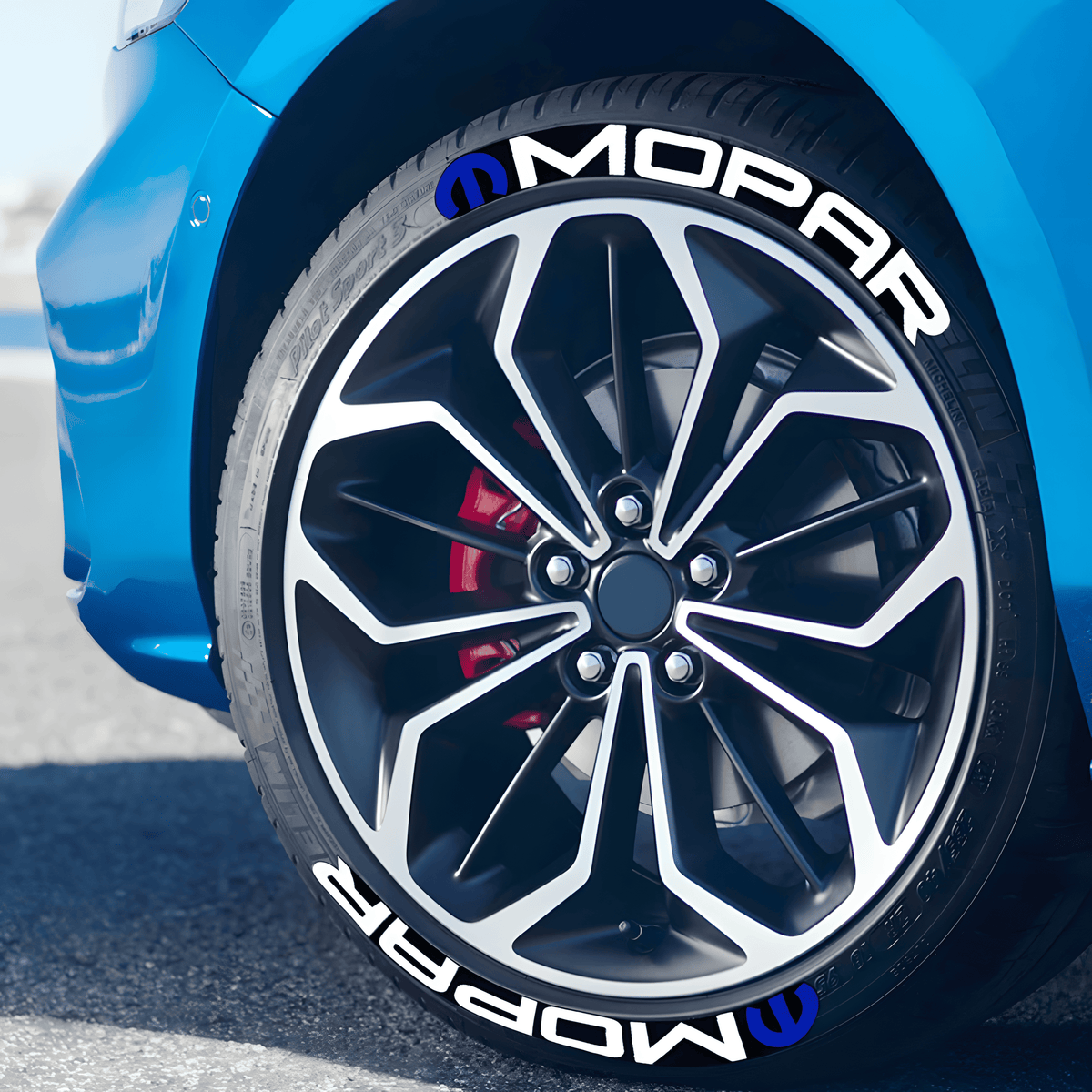 Close-up of a blue car featuring MOPAR 3D tire lettering stickers with a white logo and blue emblem applied to the tire sidewall, enhancing the sporty and customized look of the vehicle.