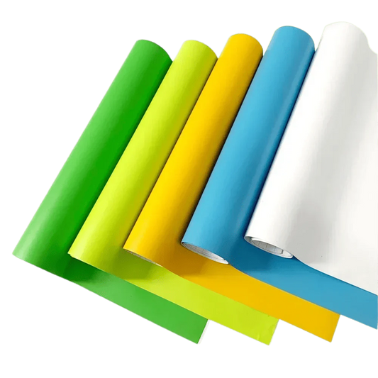A vibrant selection of ChroMorpher Matte Vinyl rolls in green, yellow, blue, and white, laid out diagonally to showcase their smooth matte texture and versatility for various customization projects.