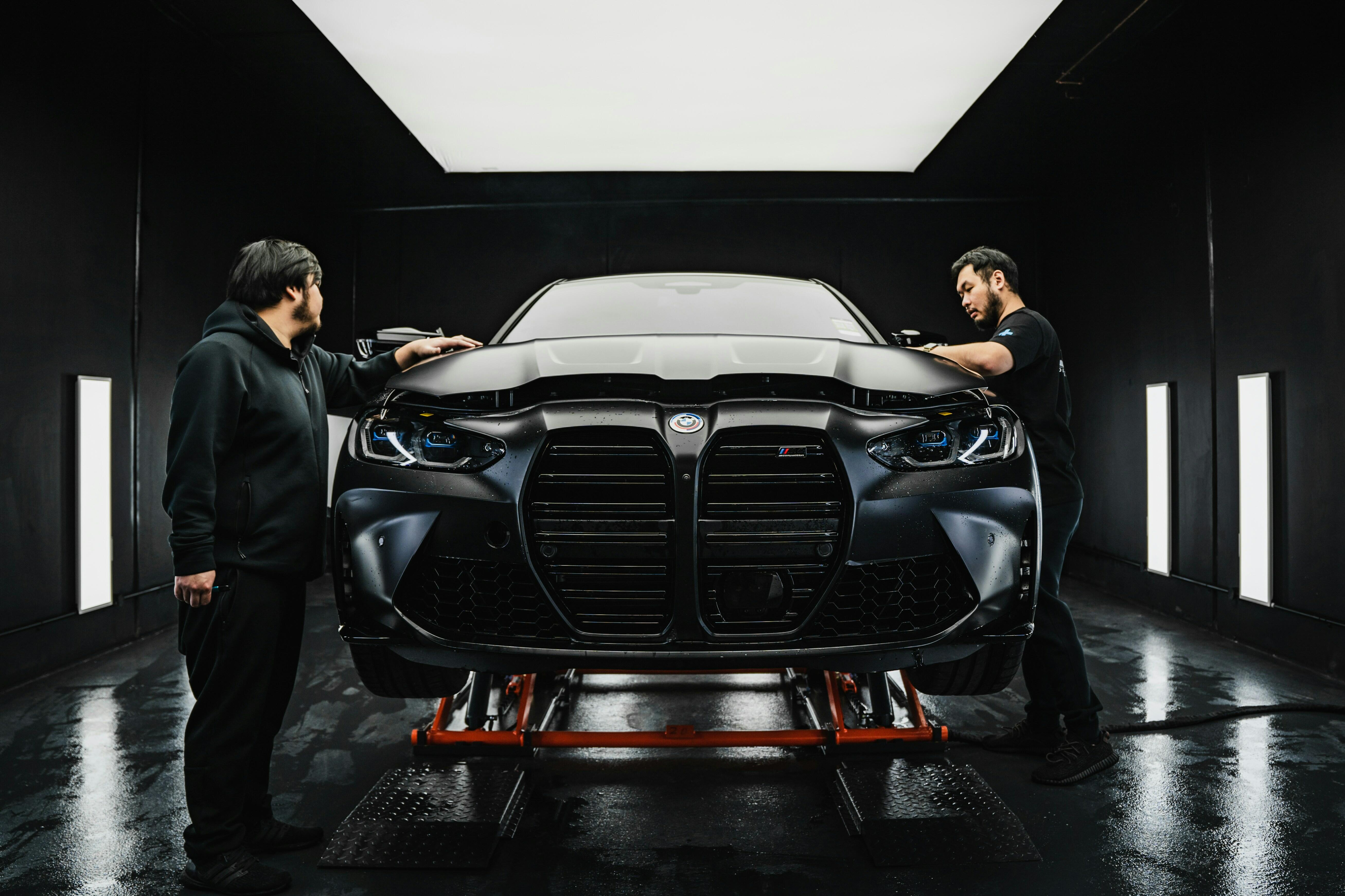 BMW M4 Detailing and Customization Two technicians working on a sleek black BMW M4 in a specialized garage, focusing on detailing and modification work.