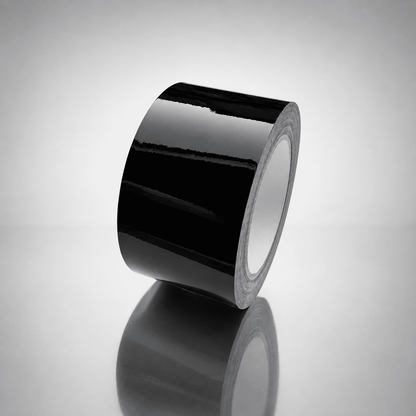 A roll of glossy black tape standing upright on a reflective light gray surface, with a soft reflection below.