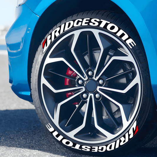 Close-up of a blue car with BRIDGESTONE 3D tire lettering stickers in white and red, applied on the tire sidewall for a bold racing-inspired look.