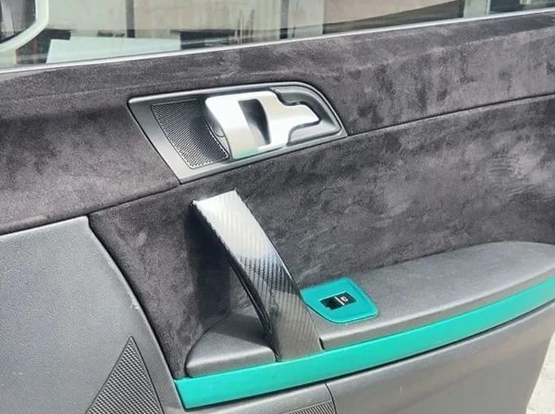 Car door interior with ChroMorpher Suede Touch Vinyl in black and vibrant turquoise accent, creating a sleek, custom look with carbon fiber trim on the door handle.