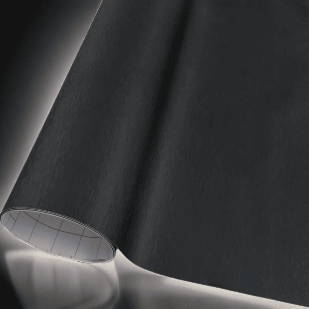 A roll of ChroMorpher brushed black vinyl wrap, showcasing a refined metallic texture with a subtle brushed finish, perfect for adding a sleek and elegant look to vehicles and various surfaces.