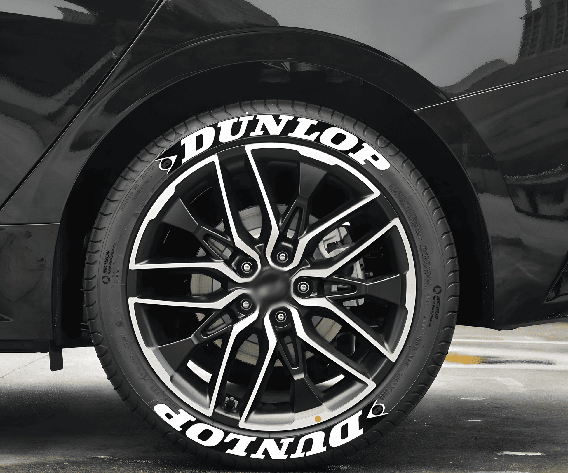 A black sports car fitted with ChroMorpher Dunlop Racing Tire Lettering Decals. The bold white "DUNLOP" text with a sleek racing-inspired design enhances the tire’s sporty look, perfect for high-performance vehicles.