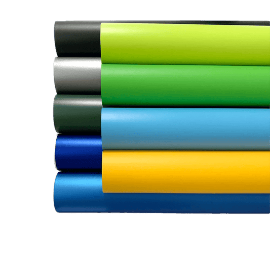 A stacked display of ChroMorpher Matte Vinyl rolls in various vibrant colors, including black, green, silver, and blue, showcasing a smooth matte finish perfect for sleek and modern surface transformations.