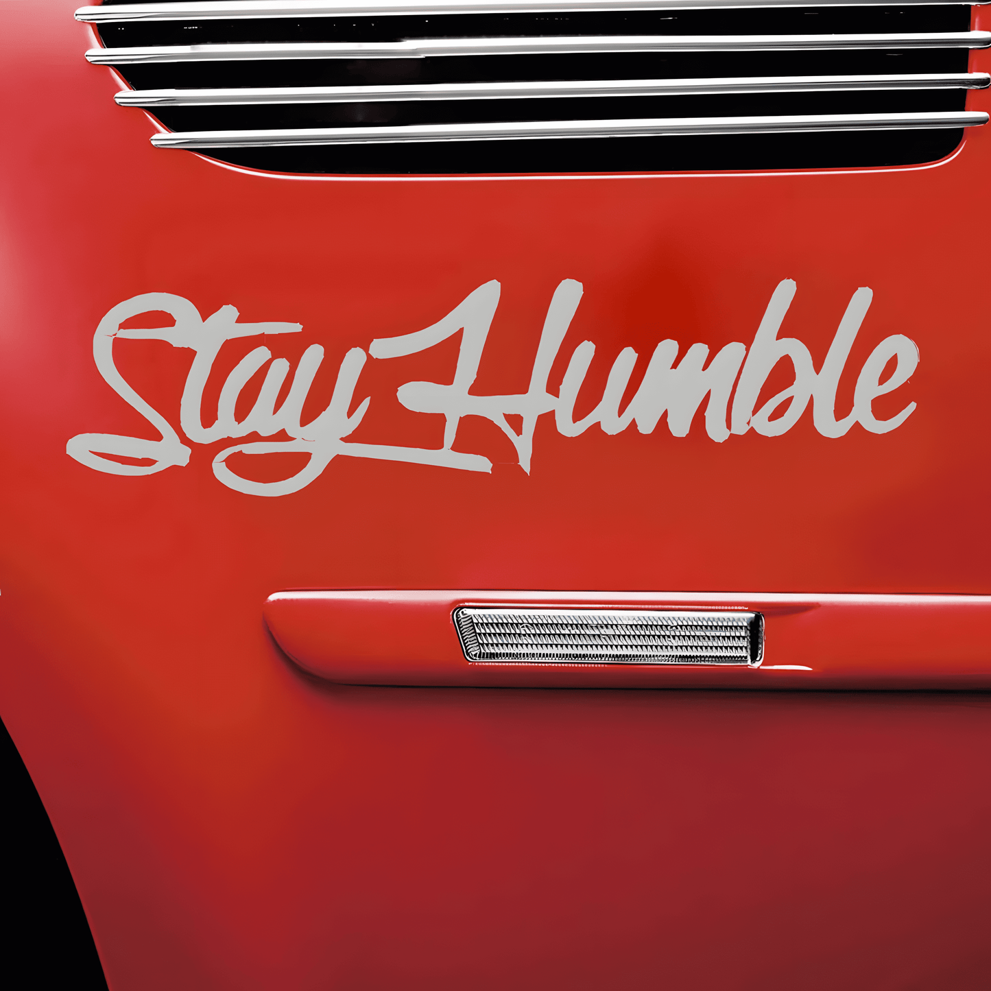 A silver-white "Stay Humble" car sticker applied to a red vehicle, featuring a glossy finish and stylish cursive font. This waterproof, self-adhesive decal is designed for car bodies, windows, bumpers, and other smooth surfaces, offering a sleek, motivational aesthetic.