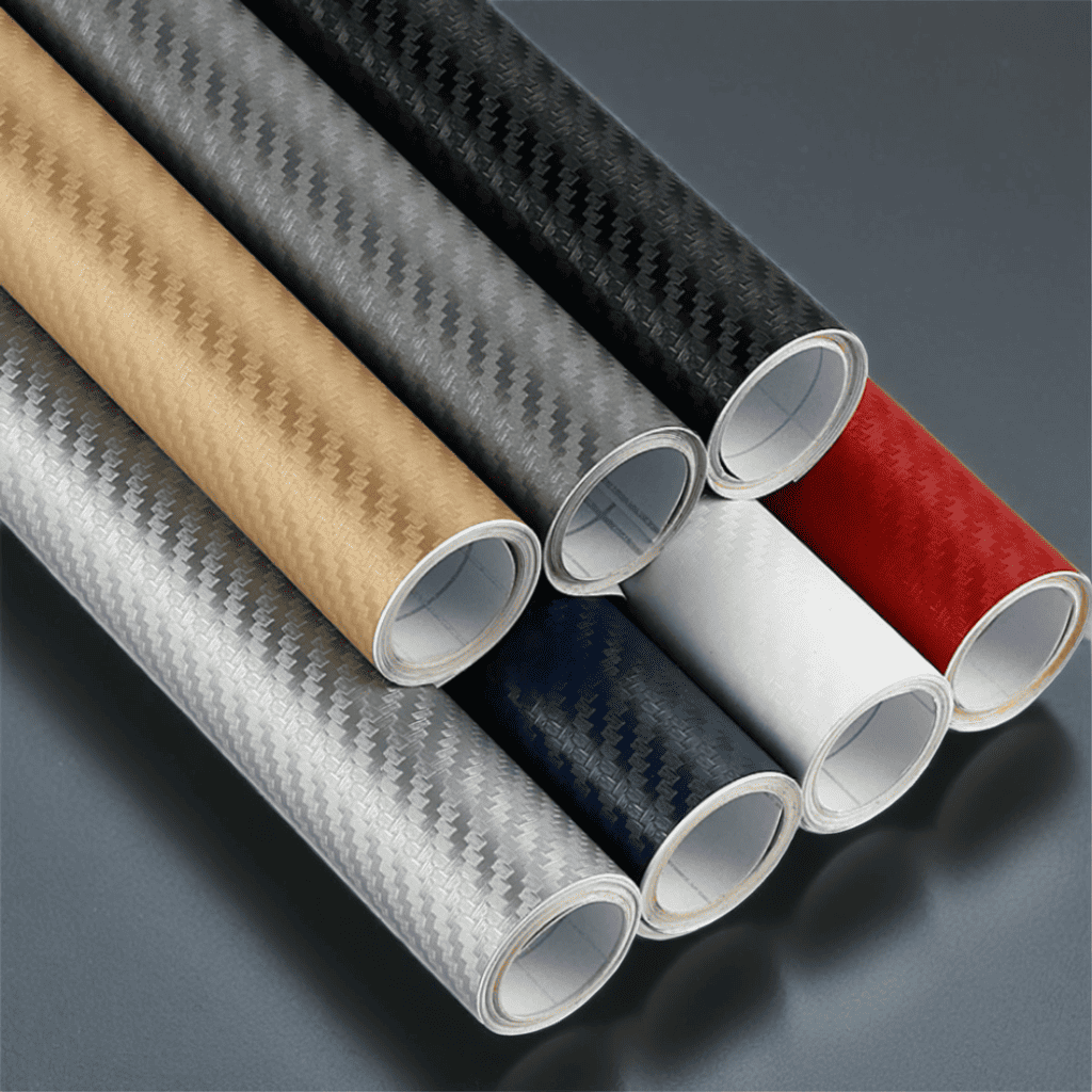 Rolls of ChroMorpher Wide Carbon Vinyls in various colors including gold, silver, black, white, red, and blue, featuring a realistic 3D carbon fiber texture. Ideal for vehicle customization and other surfaces