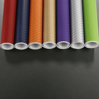 Rolls of ChroMorpher Wide Carbon Vinyls in vibrant colors including red, blue, orange, gold, purple, silver, and green, showcasing a realistic 3D carbon fiber texture for vehicle and surface customization.