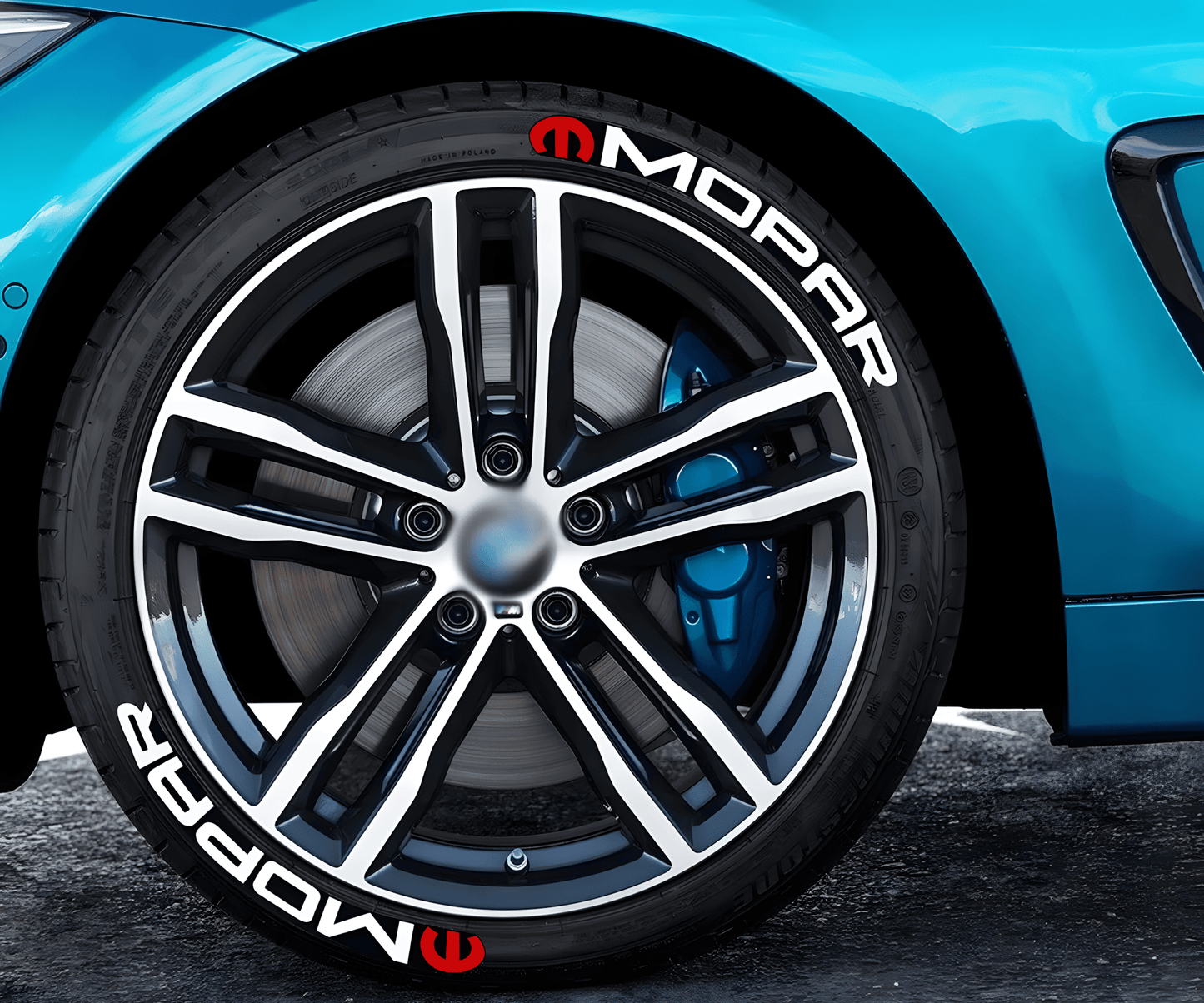 Close-up of a blue sports car with MOPAR 3D tire lettering stickers featuring a white logo and red emblem applied to the tire sidewall, adding a bold and dynamic custom touch to the vehicle's wheels.