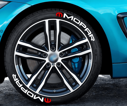 Close-up of a blue sports car with MOPAR 3D tire lettering stickers featuring a white logo and red emblem applied to the tire sidewall, adding a bold and dynamic custom touch to the vehicle's wheels.