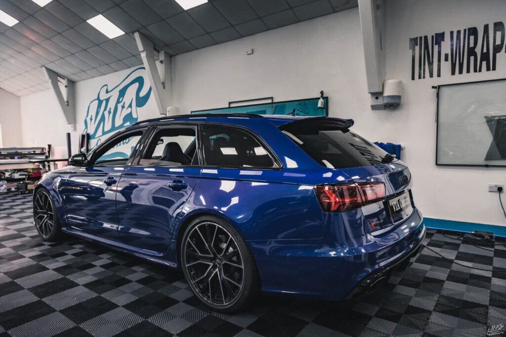 Side view of a blue Audi RS6 parked in a workshop, featuring blacked-out trim and tinted windows using ChroMorpher tape.