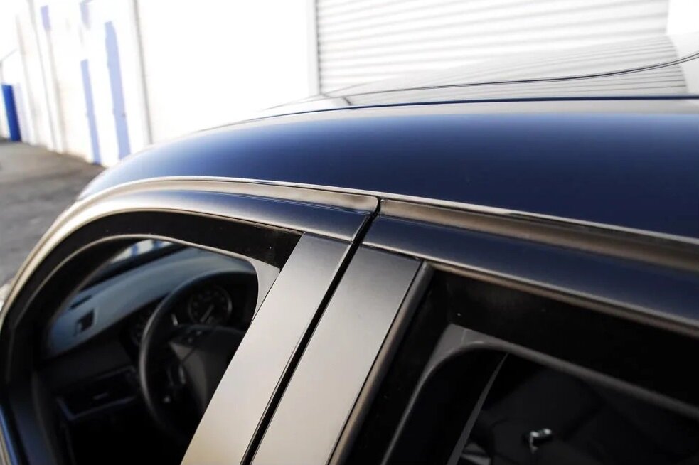 Close-up view of a car's window trim with black ChroMorpher vinyl tape applied, showcasing a seamless and clean finish.