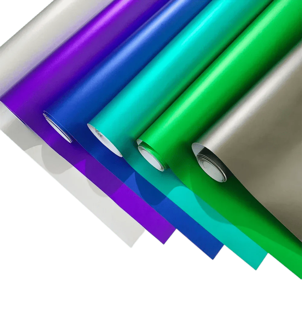 A vibrant collection of ChroMorpher Ice Matte Vinyl rolls in shades of green, gray, purple, blue, and teal, displayed with a satin matte chrome finish, ideal for vehicle wraps and DIY customization projects.