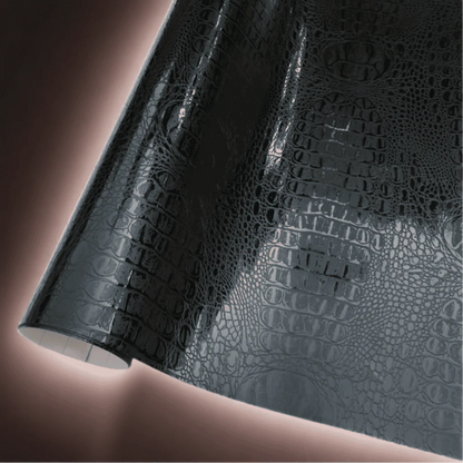 A roll of ChroMorpher black vinyl wrap featuring a glossy crocodile-skin texture, providing a luxurious and exotic finish perfect for vehicles, furniture, and custom design projects.