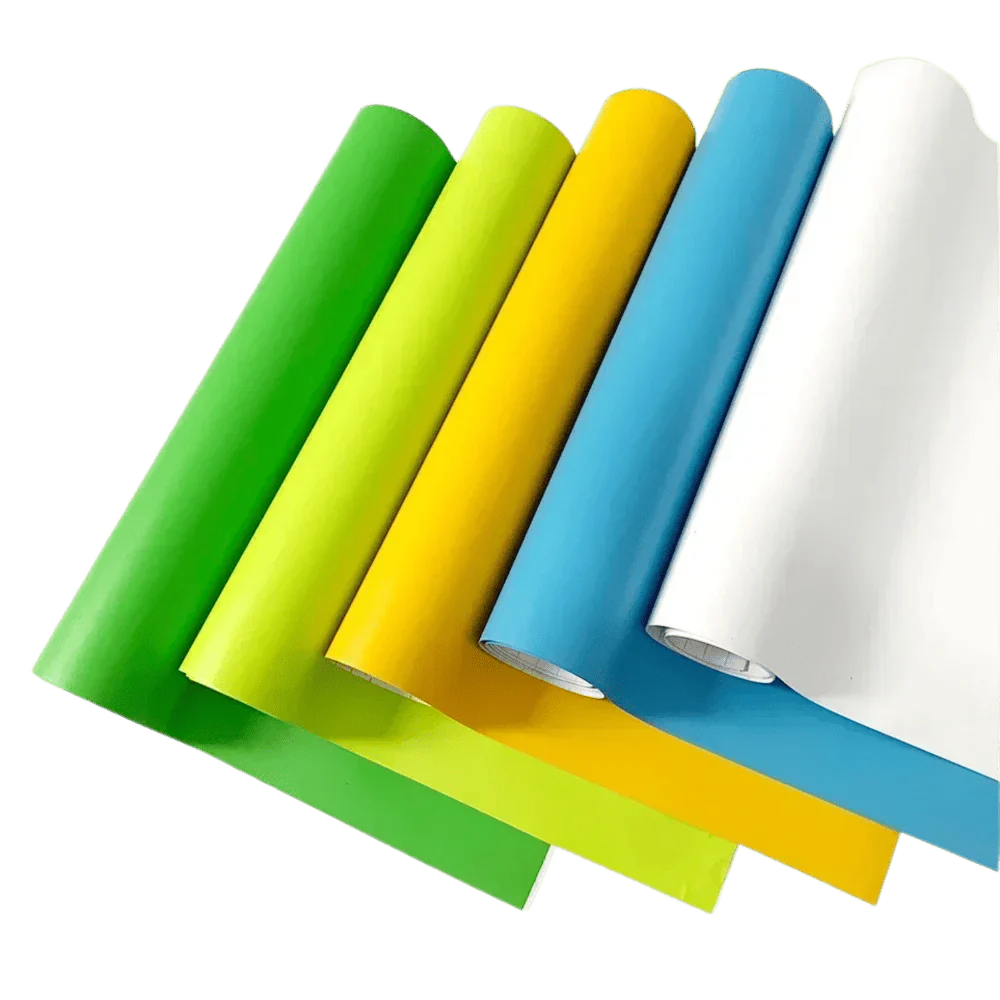 A vibrant selection of ChroMorpher Matte Vinyl rolls in green, yellow, blue, and white, laid out diagonally to showcase their smooth matte texture and versatility for various customization projects.
