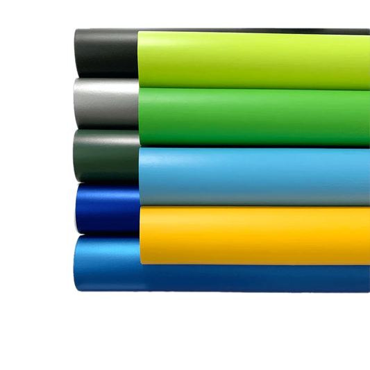 A stacked display of ChroMorpher Matte Vinyl rolls in various vibrant colors, including black, green, silver, and blue, showcasing a smooth matte finish perfect for sleek and modern surface transformations.