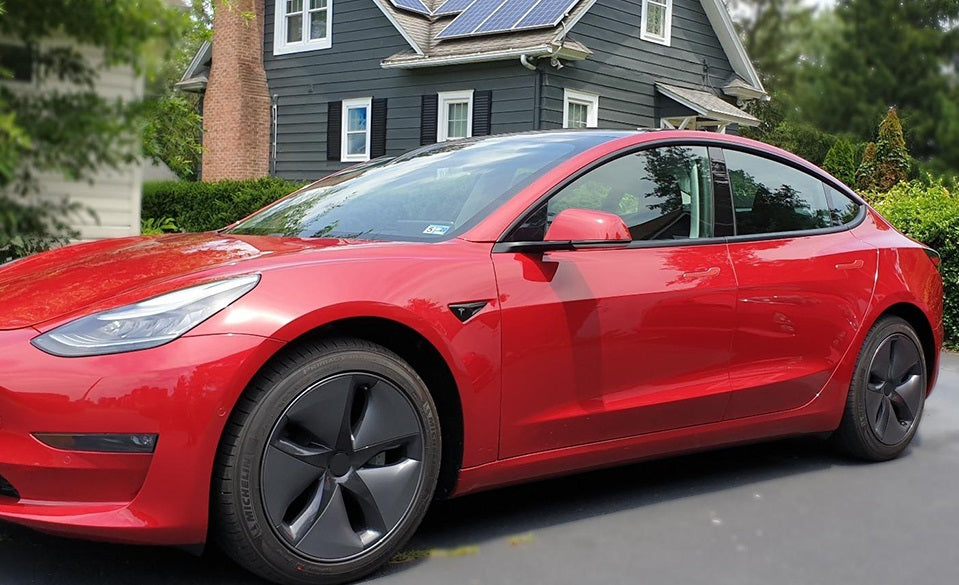 Red Tesla Model 3 parked in a driveway, featuring chrome delete on the window trims using ChroMorpher tape, enhancing its sleek appearance.