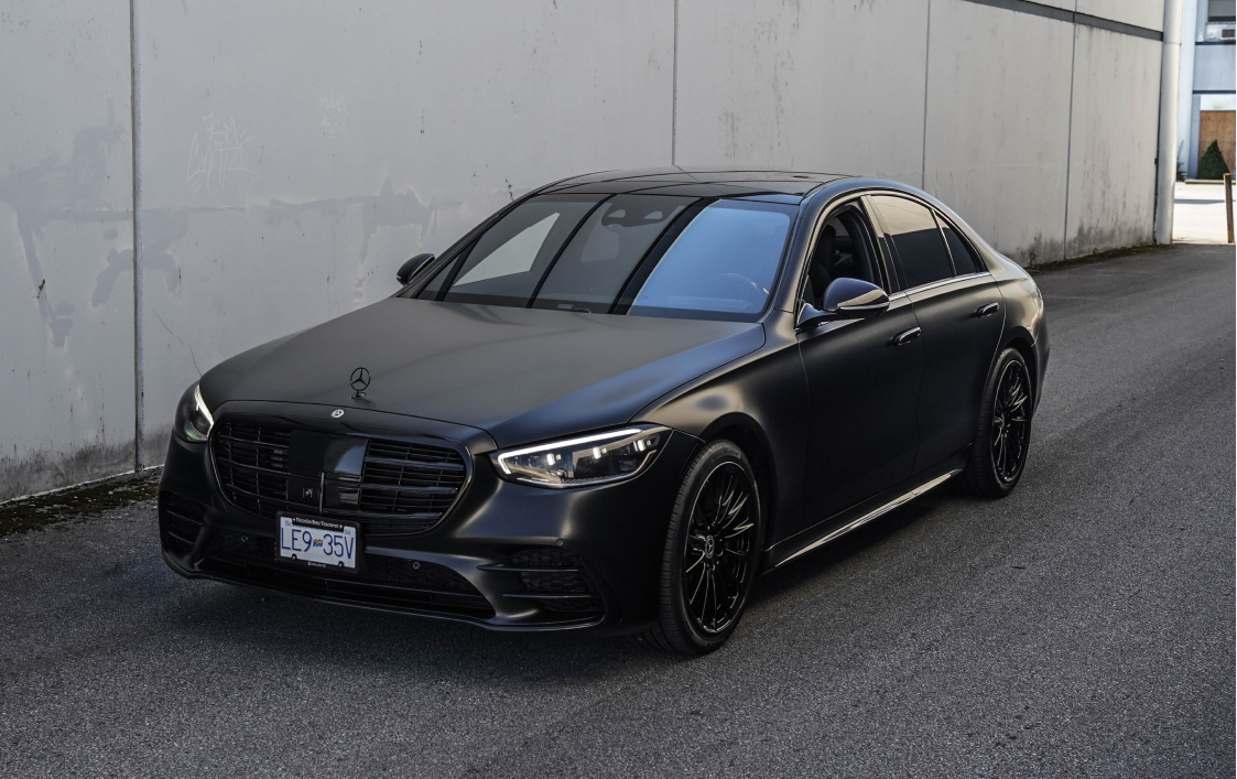 Mercedes-Benz sedan in matte black finish parked in an industrial area, featuring sleek chrome delete and blacked-out trims.