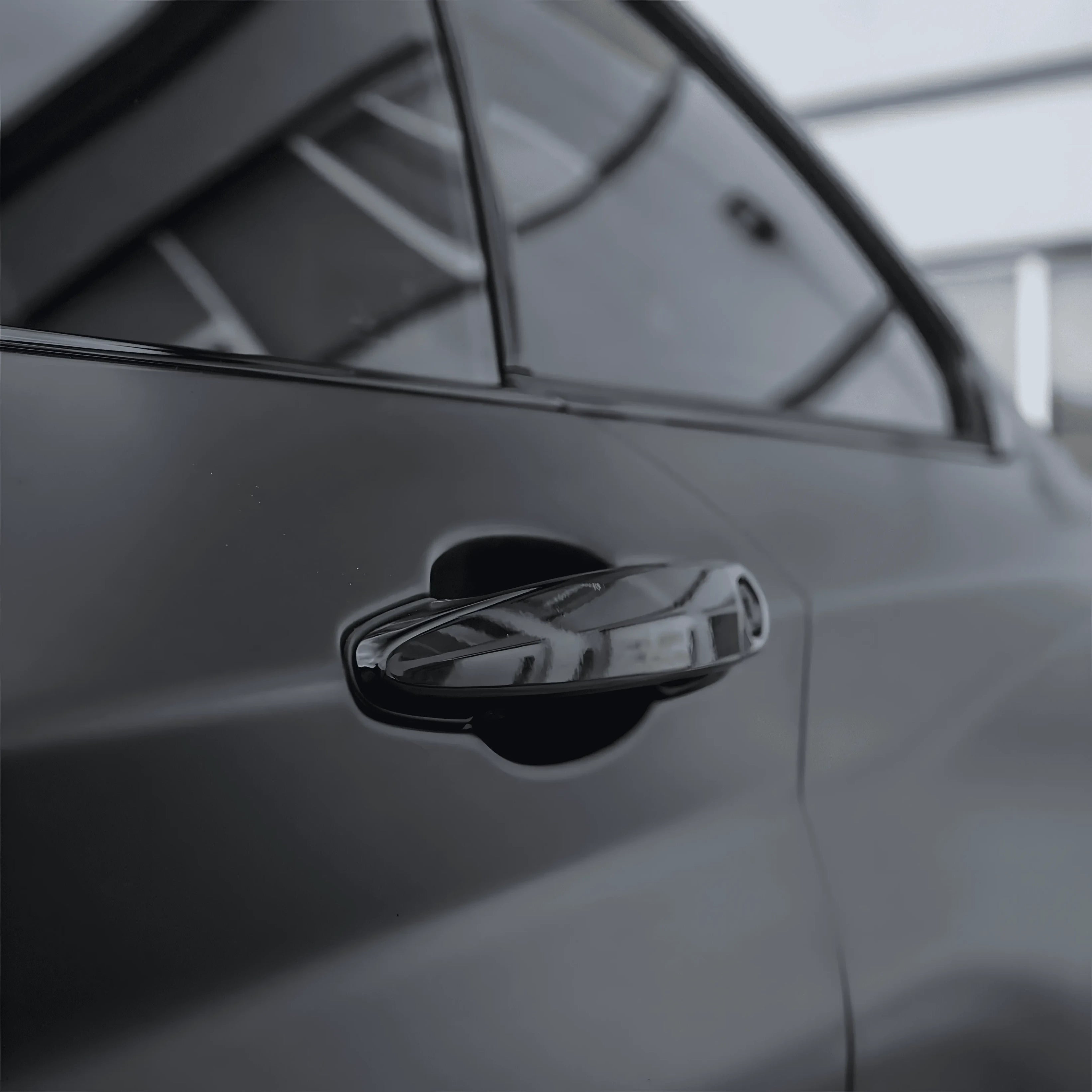 Close-up of car door handle wrapped with ChroMorpher Matte Black Chrome Delete Tape for a seamless blackout look.