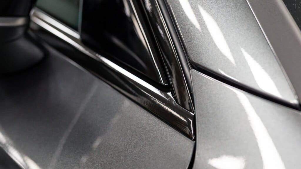Close-up of a car's side mirror and chrome-trimmed window featuring a high-gloss finish achieved with ChroMorpher Chrome Delete Tape.