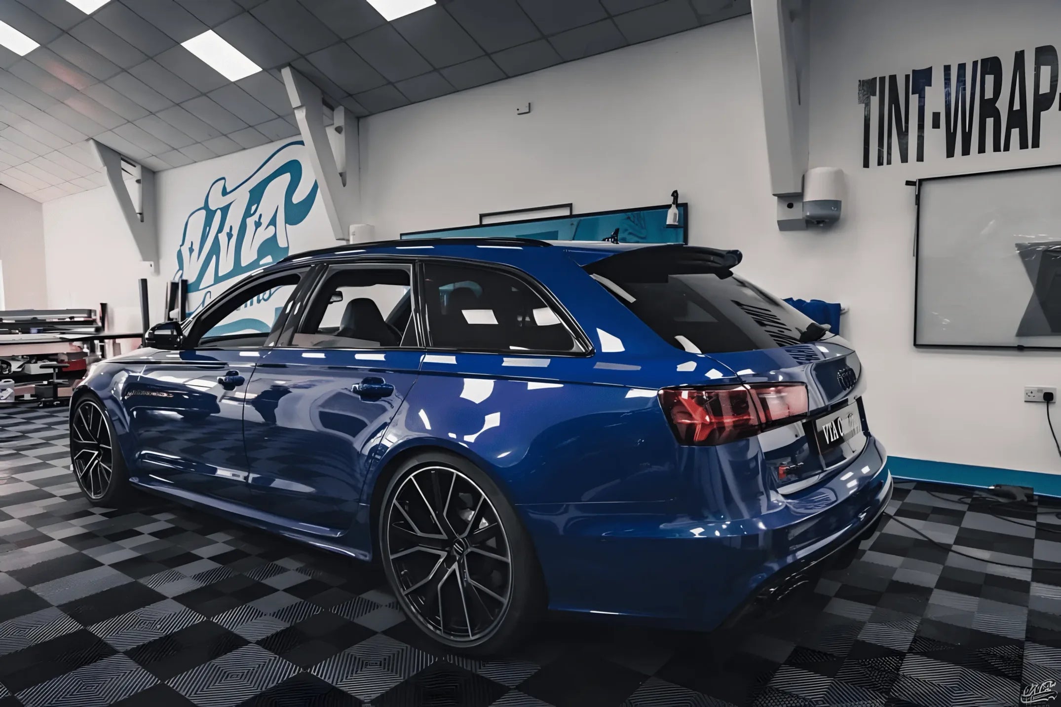 Blue Audi wagon with blacked-out window trim after applying ChroMorpher Glossy Chrome Delete Tape inside detailing shop.