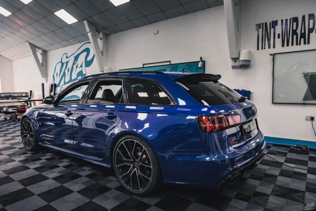 Audi RS6 Avant in a workshop after receiving a full chrome delete, including window trims, roof rails, and grilles, using ChroMorpher tape.