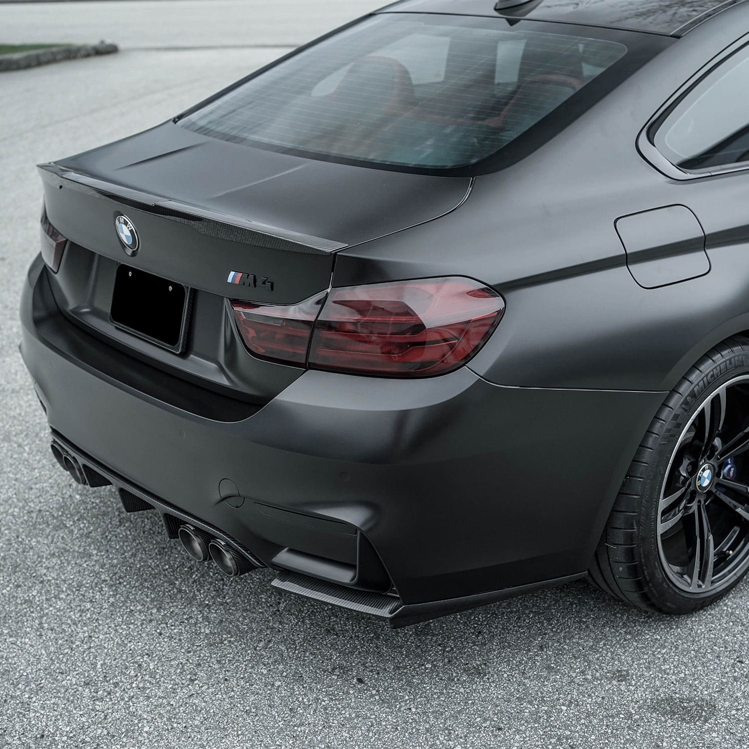 Rear view of a matte black BMW M4 showcasing dechromed taillights and trim.