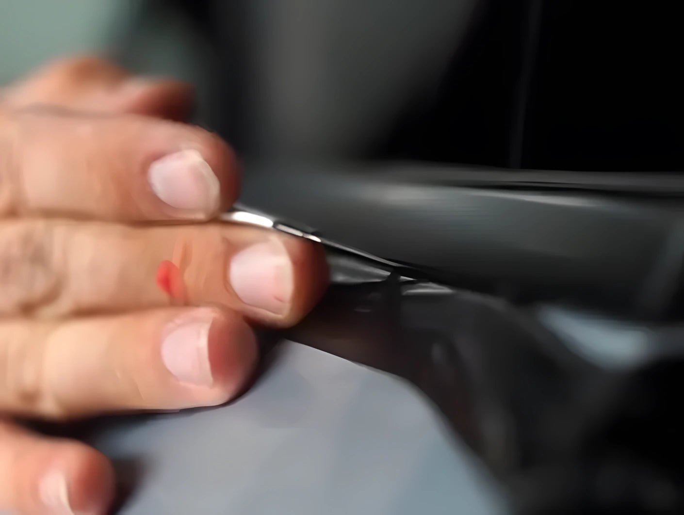 Close-up of hand applying and pressing ChroMorpher Chrome Delete Tape onto car trim during installation.