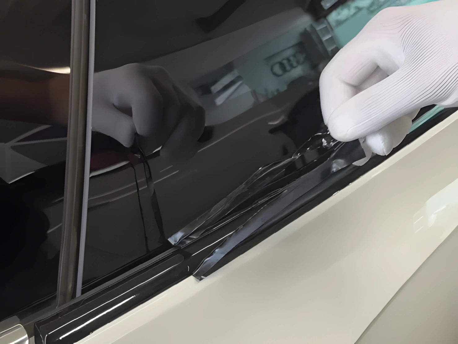 Close-up of hand applying and pressing ChroMorpher Chrome Delete Tape onto car trim during installation.