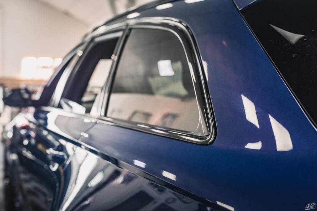 Close-up view of a car's glossy black window trim after chrome delete application, reflecting a smooth, professional finish.